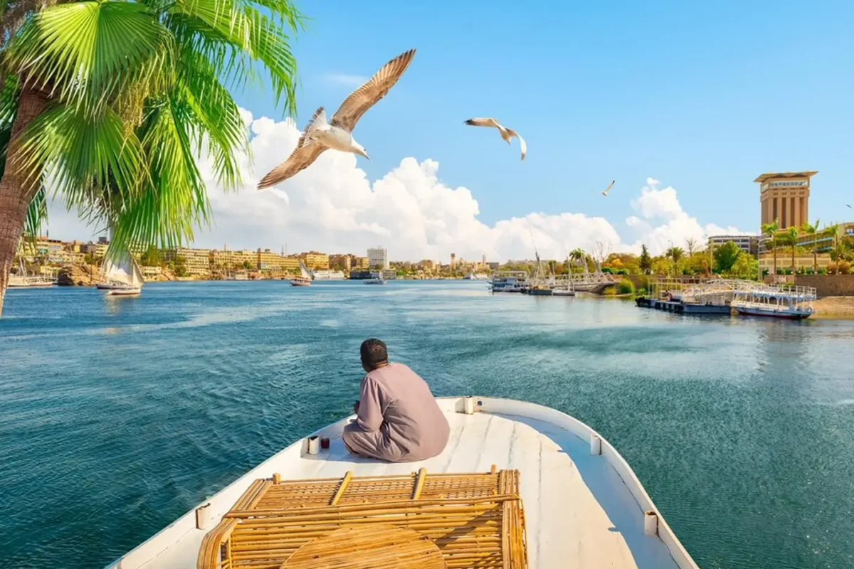 A man in a white galabeya sitting at the stern of a boat sailing the Nile at Aswan