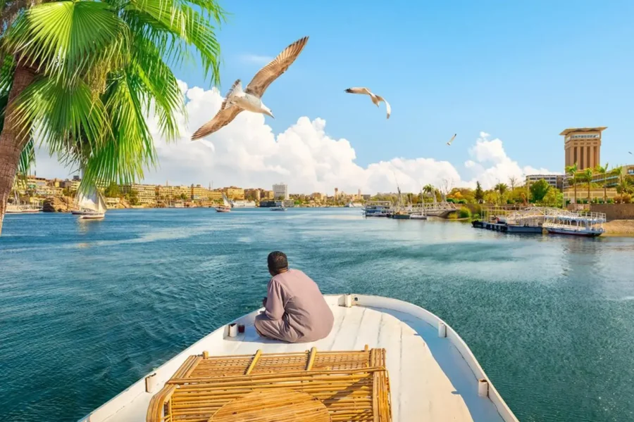 A man in a white galabeya sitting at the stern of a boat sailing the Nile at Aswan