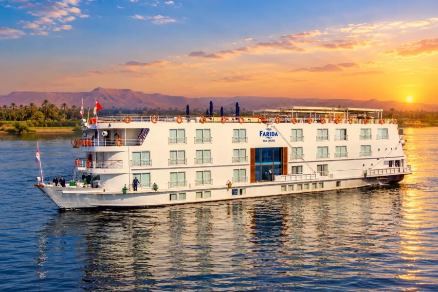 The Farida Nile cruise ship on the Nile at sunset, the sun low behind hills on the far bank