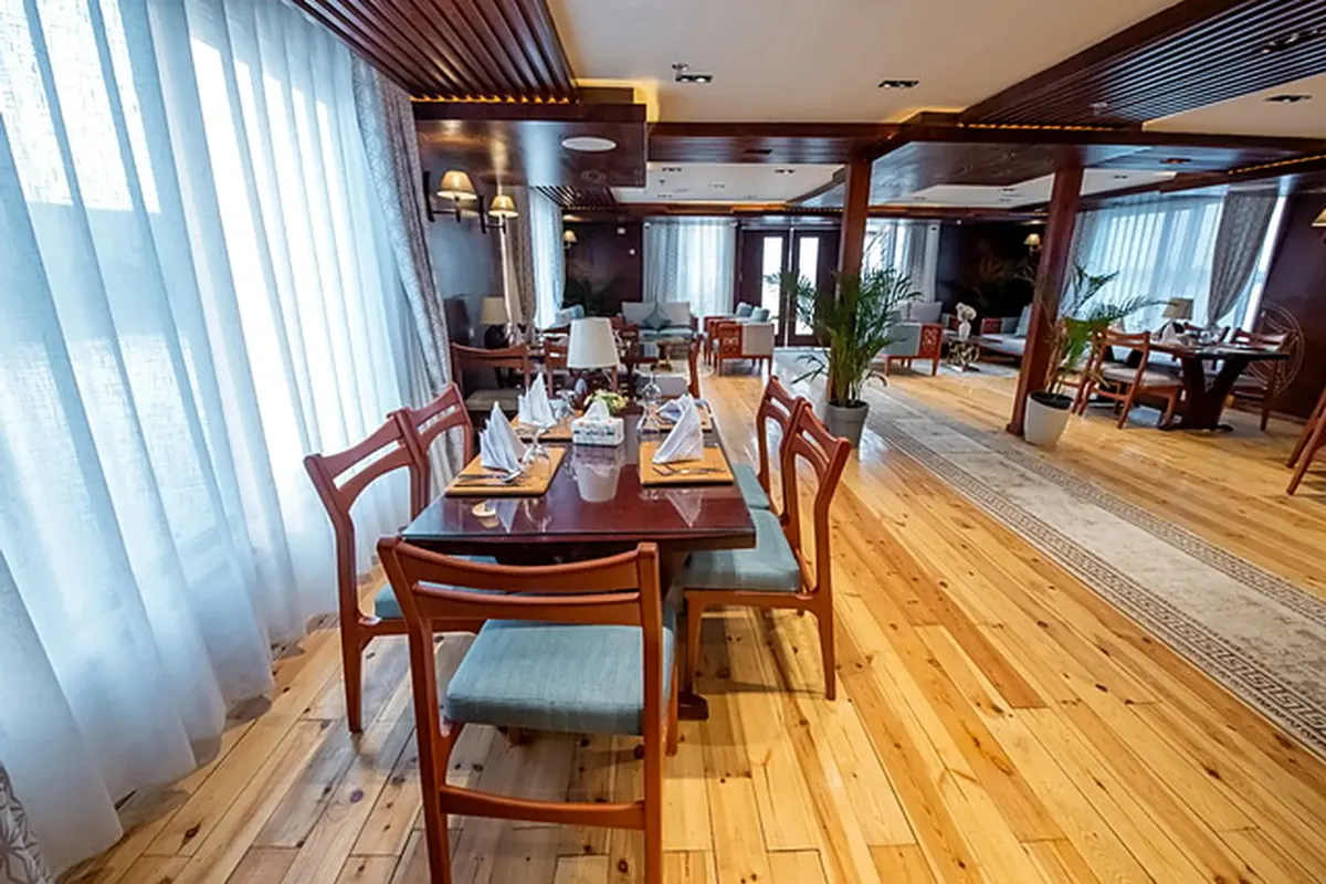 Das Restaurant der Dahabiya Azhar, Tische auf Holzboden neben Fenstern mit Vorhängen