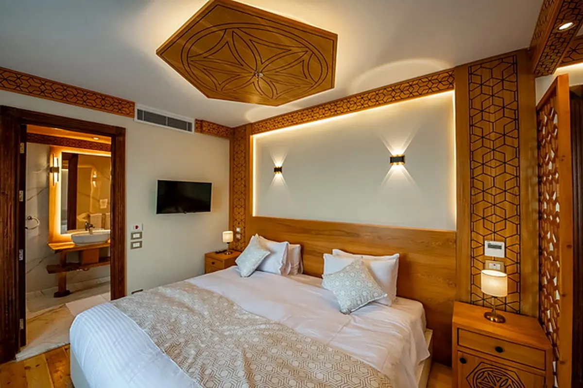 Eine Suite auf der Dahabiya Azhar mit Doppelbett, einem geschnitzten Holzmedaillon an der Decke und dem Bad hinter der offenen Tür