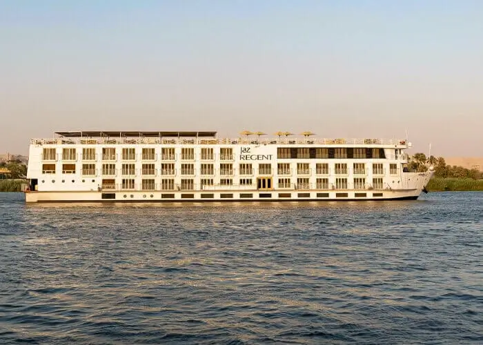 The MS Jaz Regent Nile cruise ship broadside on the Nile, its name lettered on the cream superstructure with reeds along the far bank