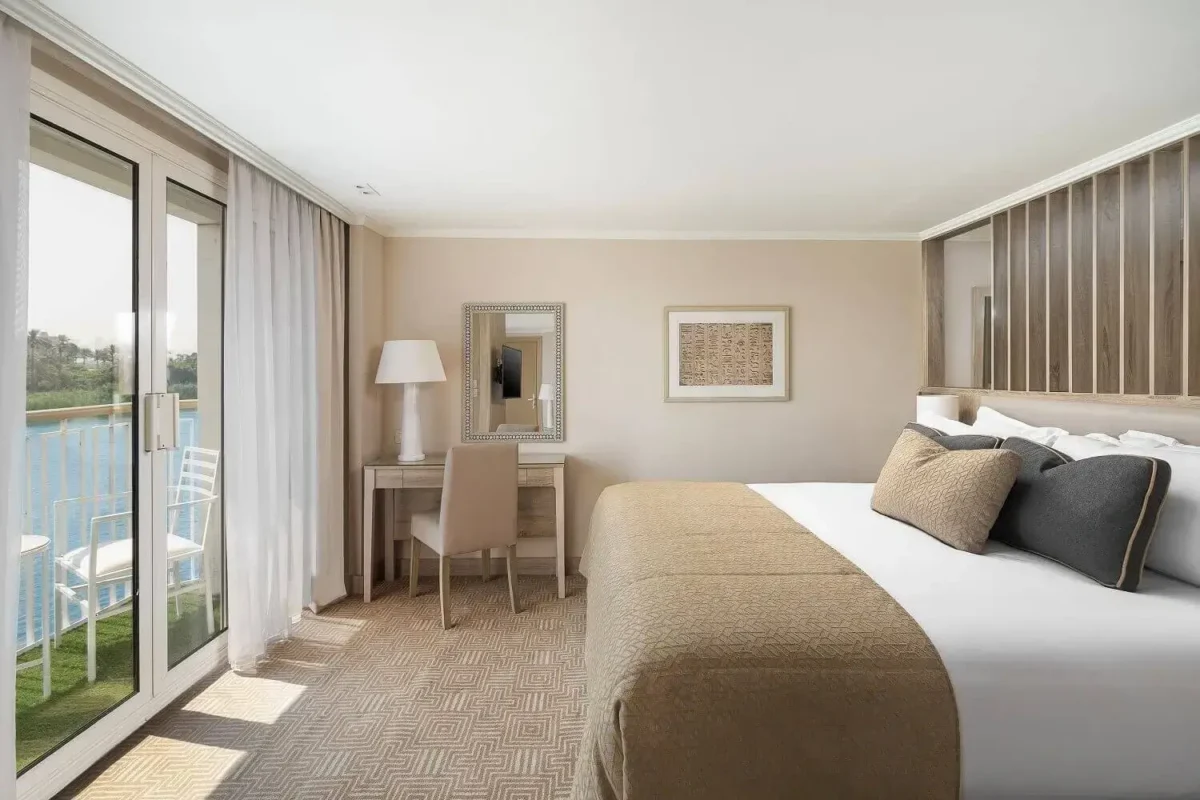 A cabin on the MS Jaz Viceroy Nile cruise in cream and grey, a glass door beside the bed opening onto the river