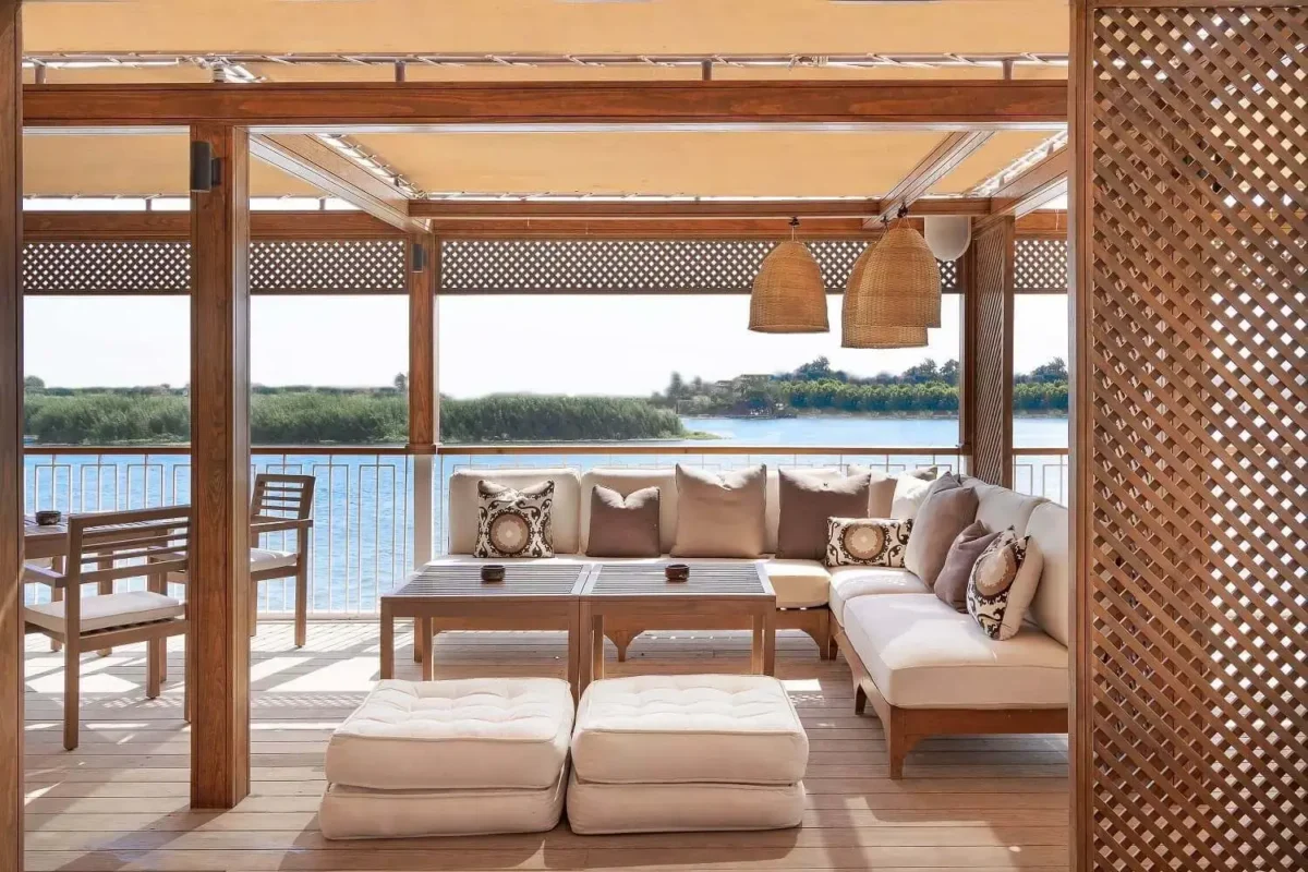 A cushioned daybed and ottomans on the MS Jaz Viceroy Nile cruise deck, looking out over the Nile to a reeded bank