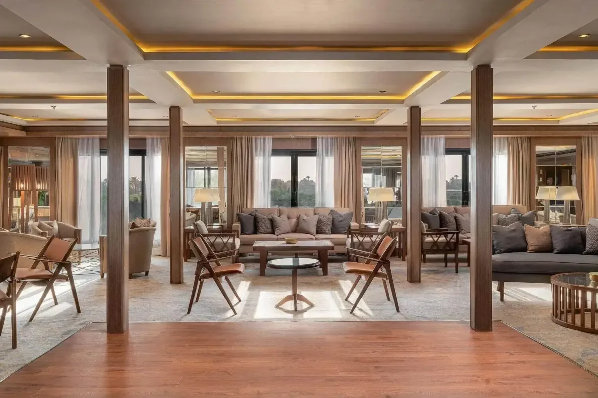 The lounge on the MS Jaz Viceroy Nile cruise, sofas and cane chairs beneath timber columns with river windows behind