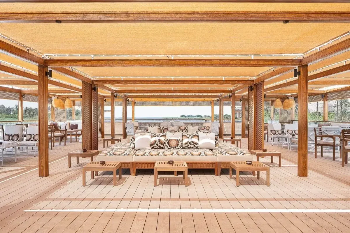 Timber daybeds under a slatted pergola on the MS Jaz Viceroy Nile cruise deck, the river visible at the far end