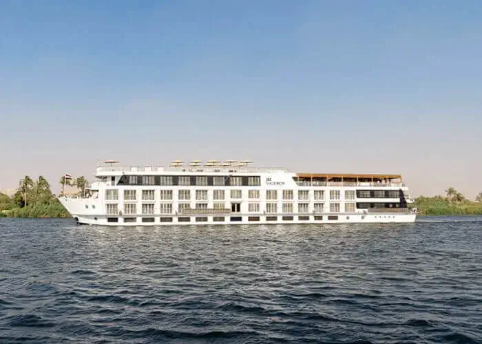 The MS Jaz Viceroy Nile cruise ship broadside on the Nile, a low green bank and palms stretching behind it