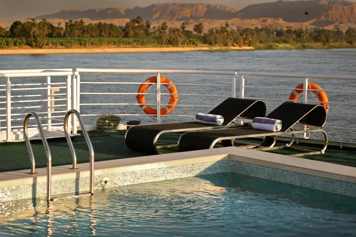 The pool on the MS Le Fayan Nile cruise deck, two loungers beside it and life rings on the rail above the river