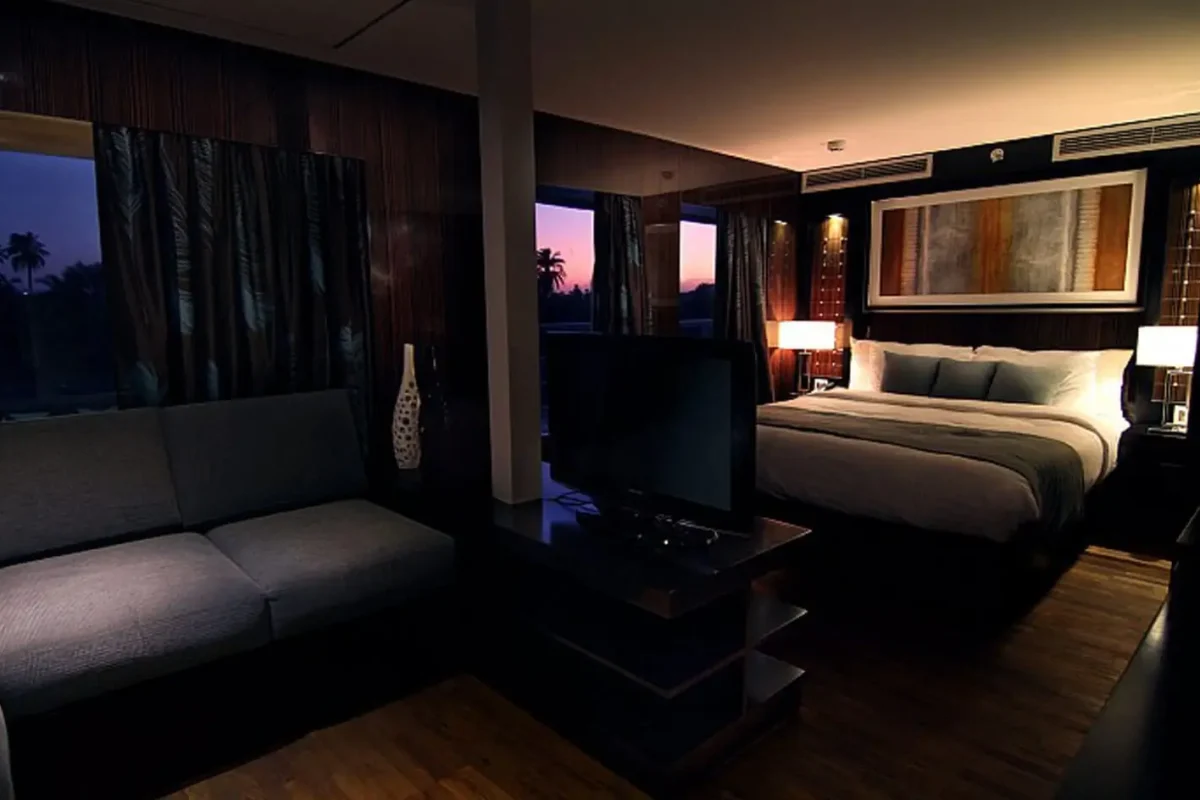 A suite on the MS Le Fayan Nile cruise at dusk, a dark sofa and television facing the bed with the river through the window