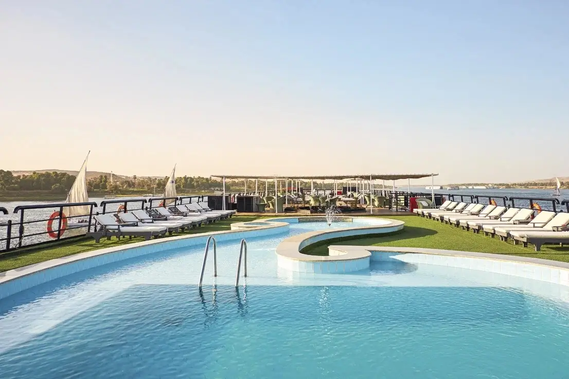 The curved swimming pool on the Movenpick MS Hamees Nile cruise sun deck in evening light, loungers set out down the length of the deck