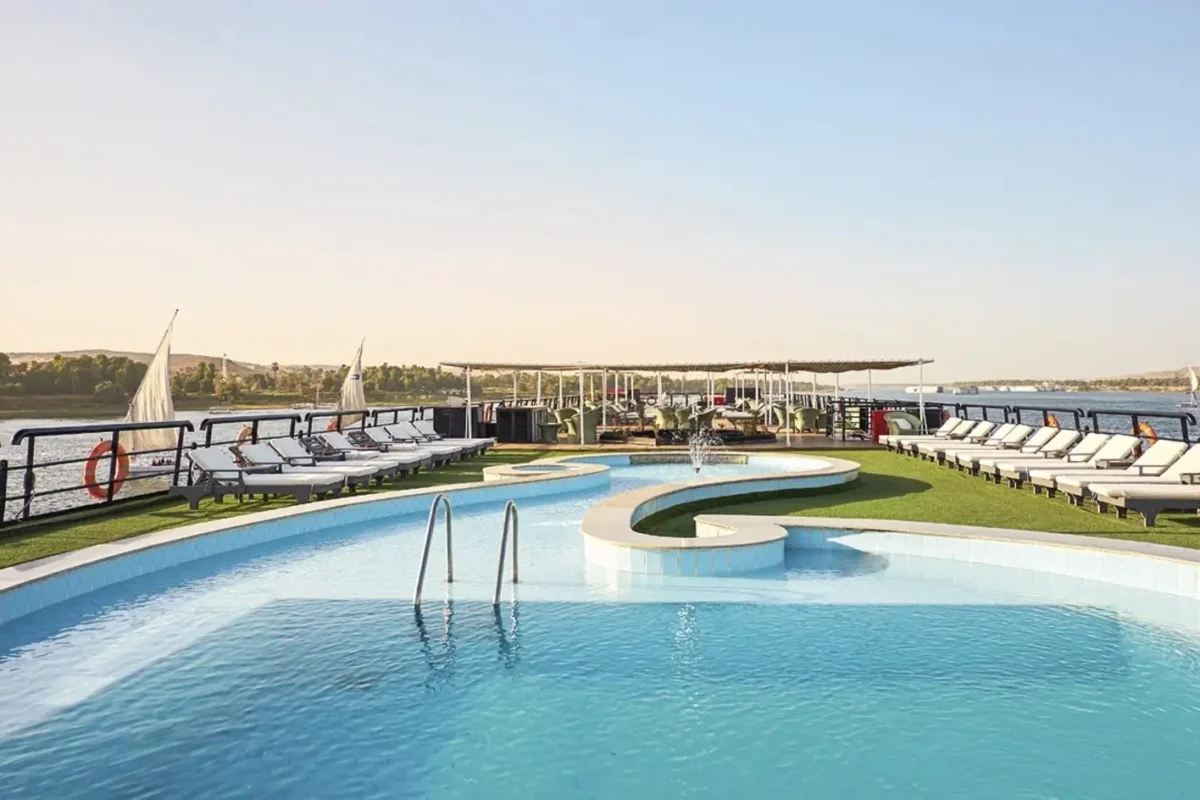 The swimming pool on the Movenpick MS Hamees Nile cruise sun deck, loungers on green lawn along both sides and feluccas on the river beyond