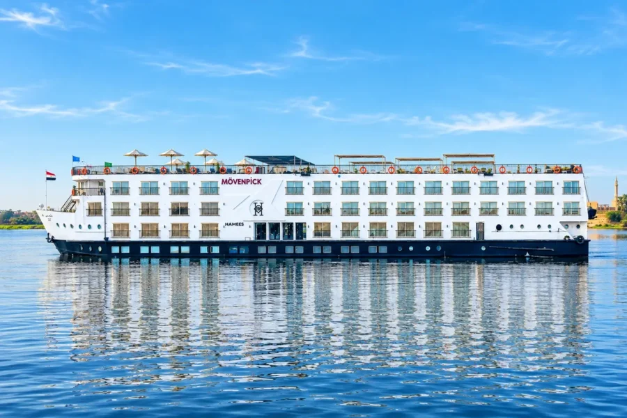 The Movenpick MS Hamees Nile cruise ship broadside on still water, its name along the upper deck and its reflection beneath it