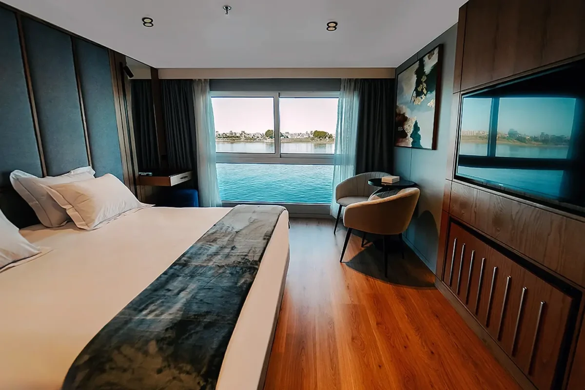 A cabin on the MS Miriam Nile cruise with a dark timber floor, a wide bed and a long window looking straight onto the Nile