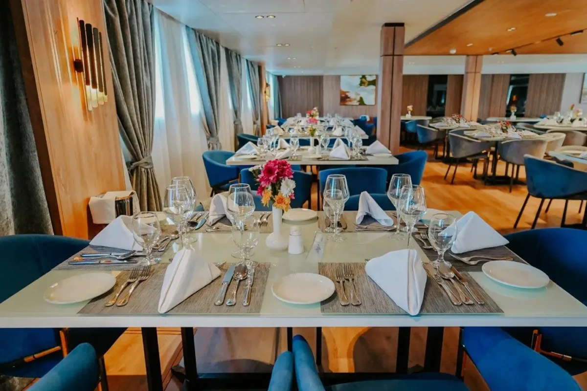 Tables laid with white linen and blue chairs in the MS Miriam Nile cruise restaurant, flowers on each table