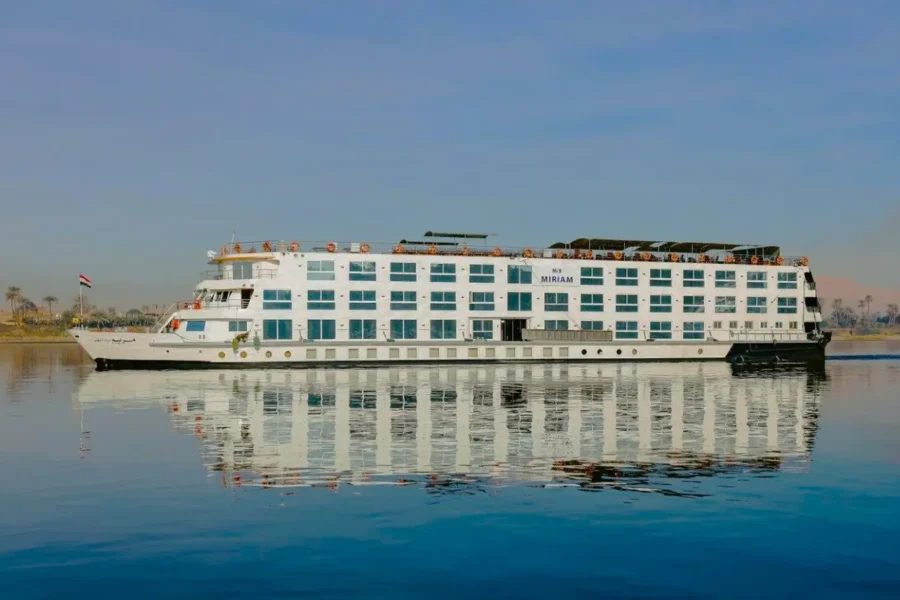 The MS Miriam Nile cruise ship on still water, its white hull and blue window bands mirrored below