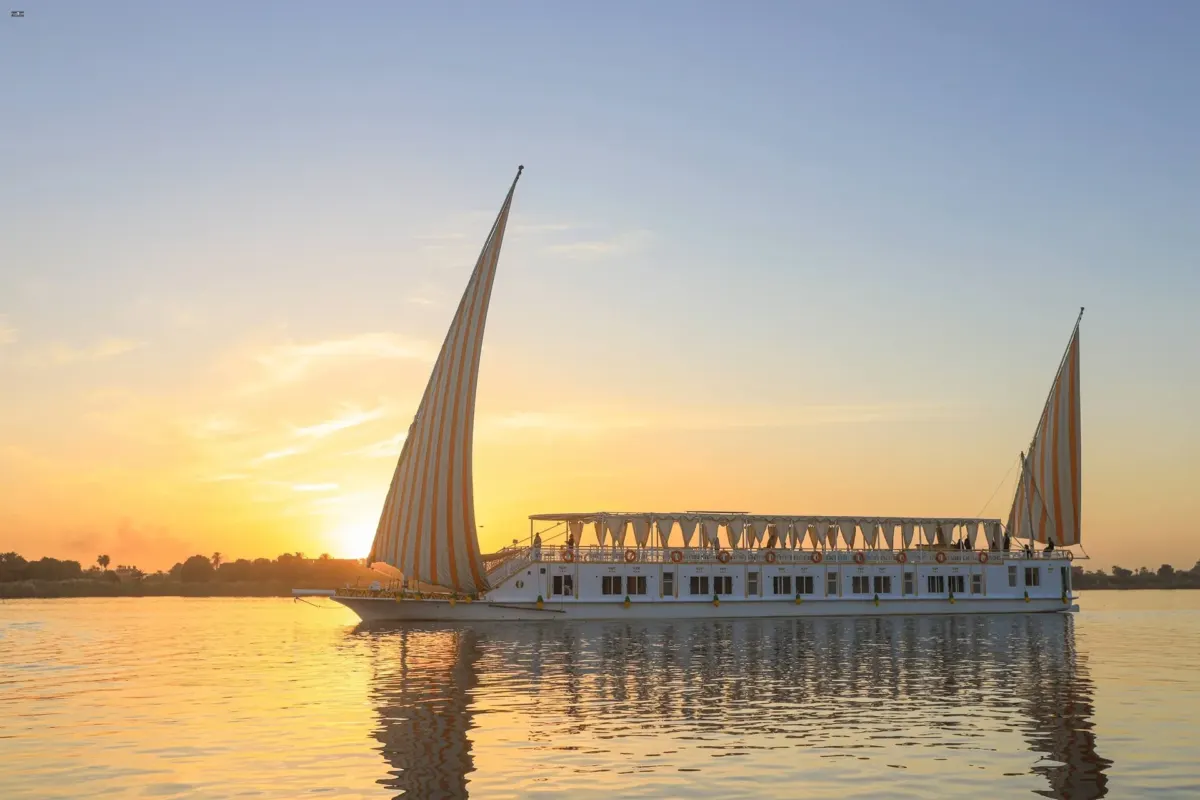 La dahabiya Nile Palace en el Nilo al atardecer, con el sol bajo tras sus velas