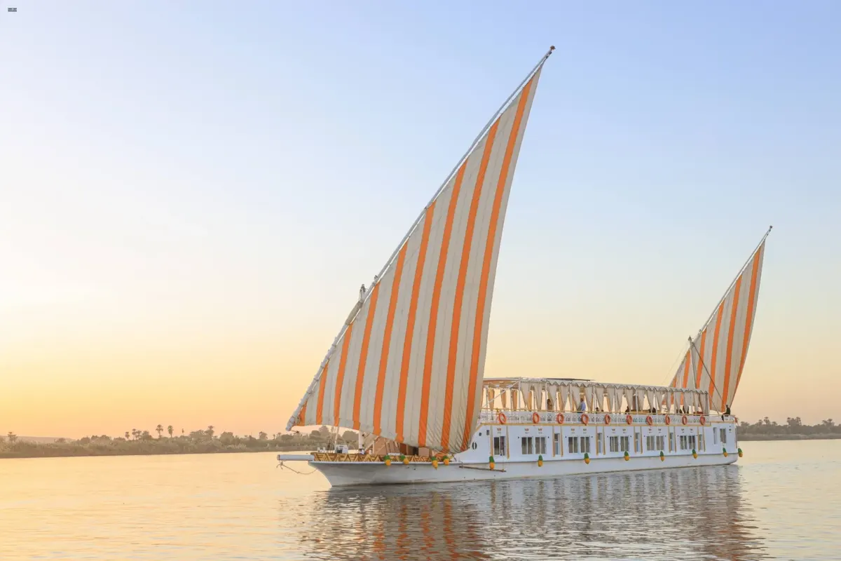 La dahabiya Nile Palace con velas rayadas en aguas tranquilas, bajo la luz de la tarde