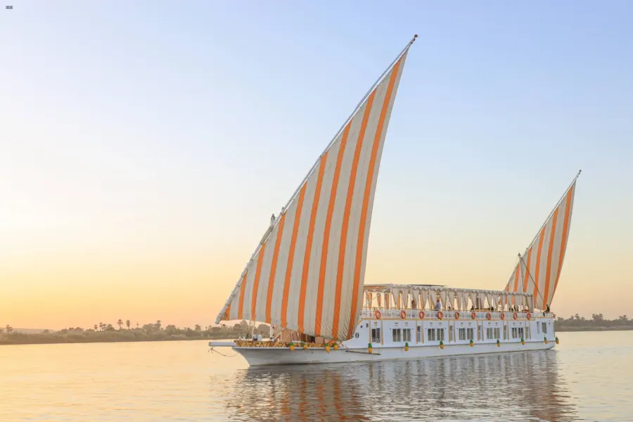 La dahabiya Nile Palace con velas rayadas en aguas tranquilas, bajo la luz de la tarde