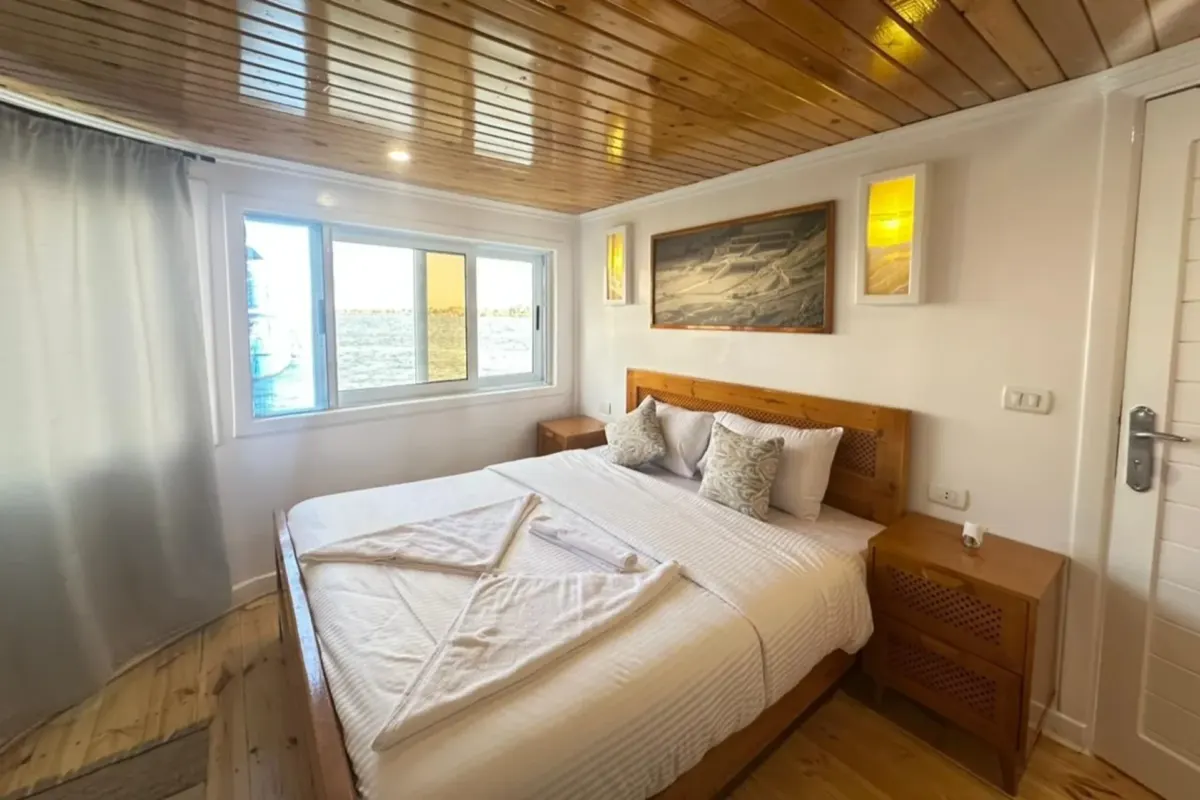 Eine Kabine auf der Dahabiya Nour El Din mit Doppelbett, Holzdecke und Fenster zum Fluss