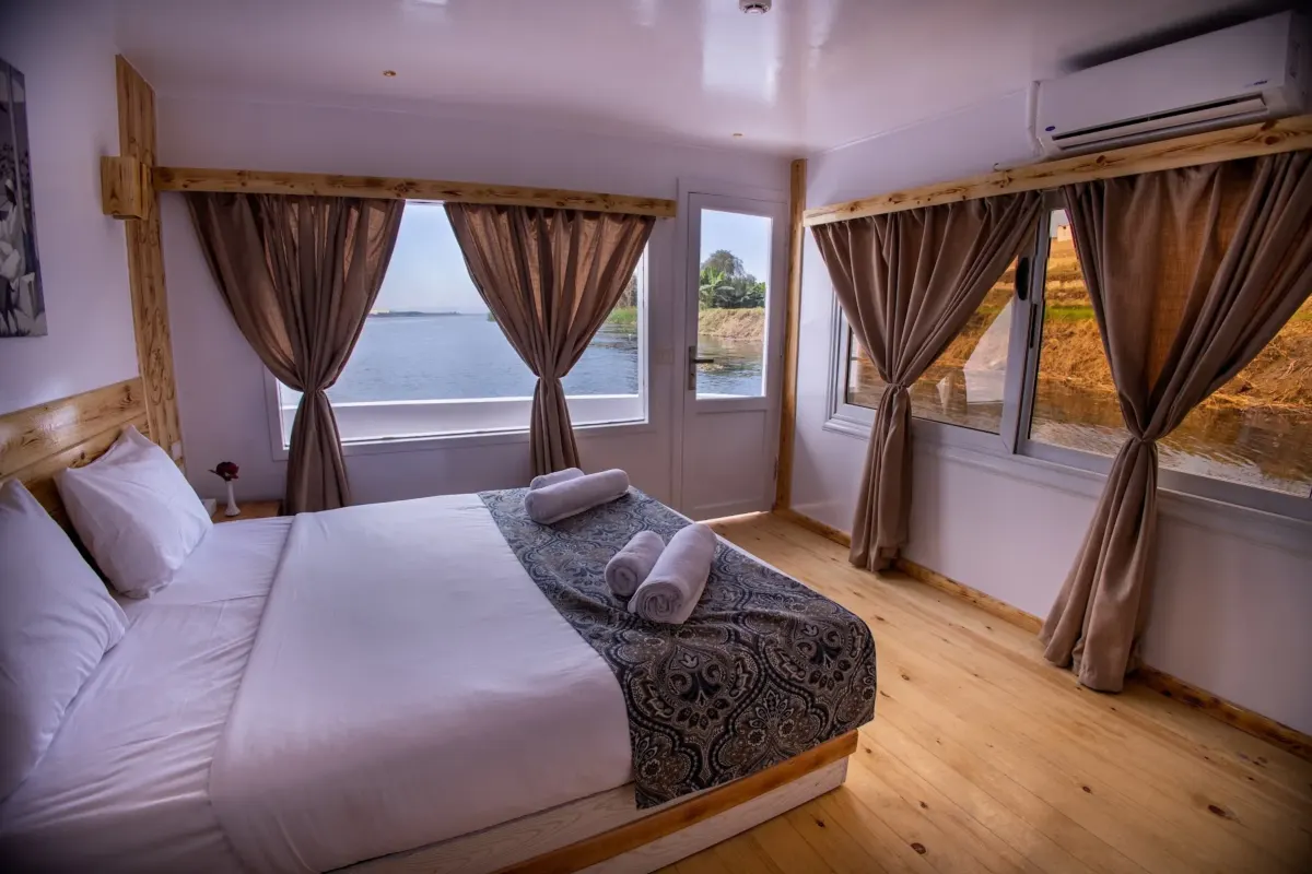 Eine Kabine auf der Dahabiya Princess Cleopatra mit Doppelbett, Holzboden und Fenstern auf zwei Seiten mit Blick auf den Nil