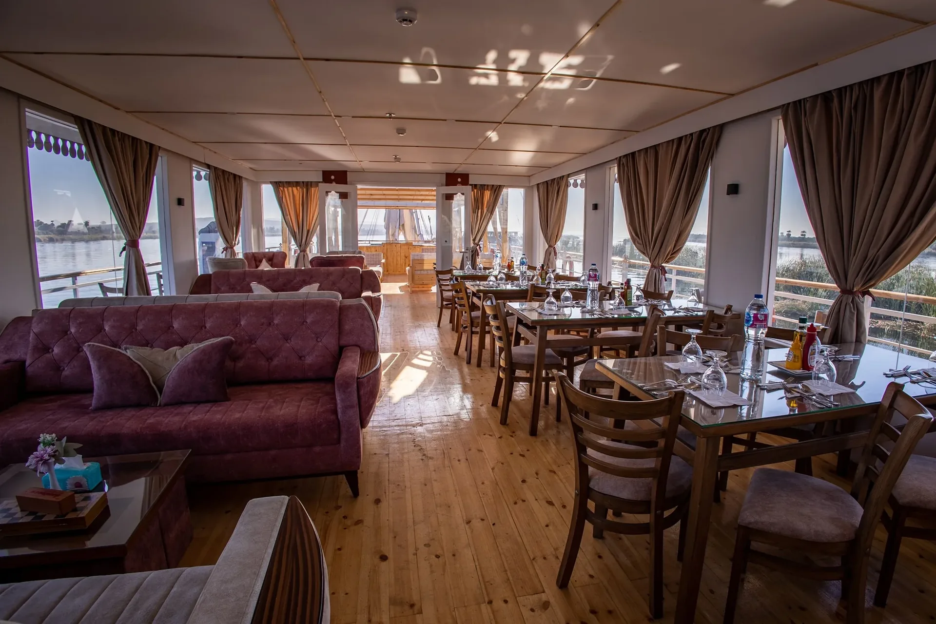 Restaurant und Lounge der Dahabiya Princess Cleopatra, Esstische neben Fenstern mit Vorhängen