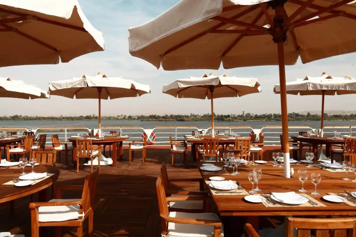 Tables laid under cream parasols on the open deck of the Sonesta Nile Goddess Nile cruise, the river beyond