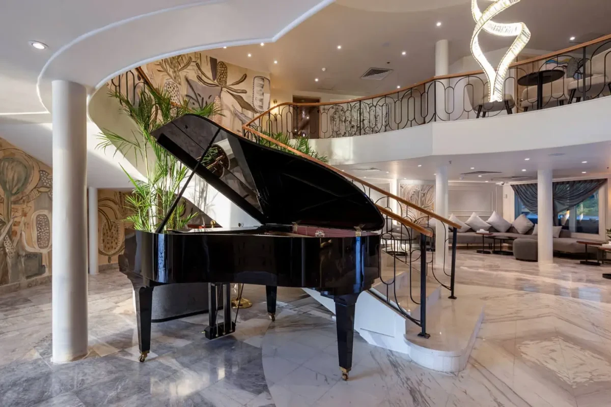 A grand piano beneath the curved balcony of the Sonesta Nile Goddess Nile cruise lounge, a painted mural on the wall behind