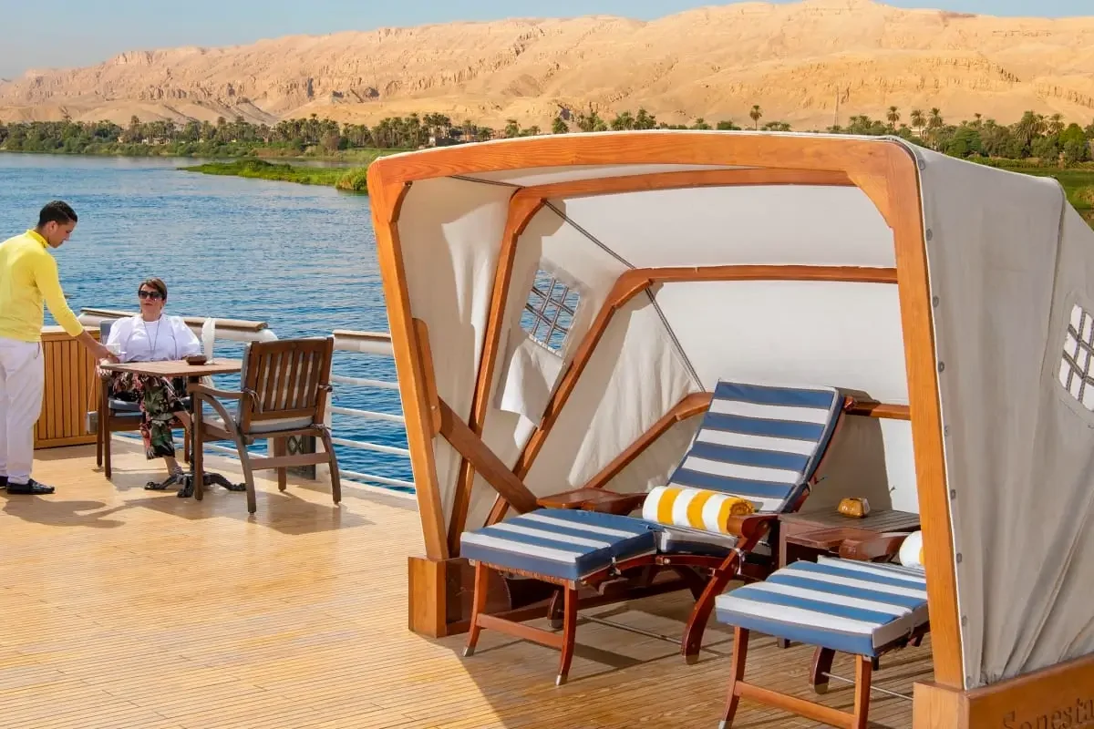 A canopied daybed and a table set for breakfast on the Sonesta St. George I Nile cruise deck, the Nile and hills beyond
