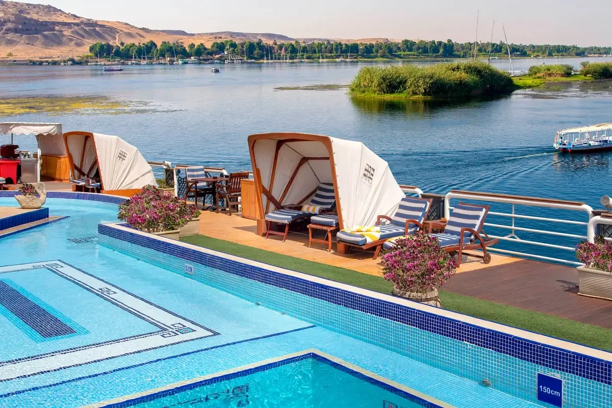 The swimming pool on the Sonesta St. George I Nile cruise sun deck, shaded daybeds along the rail above the river