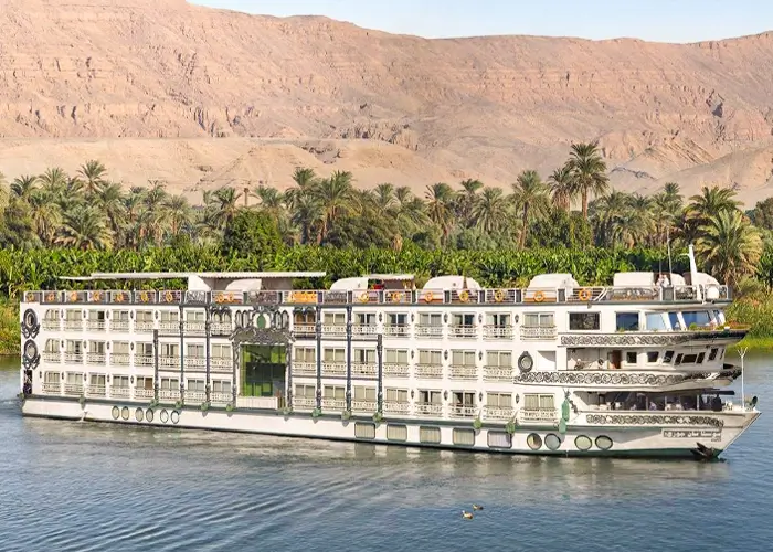 The Sonesta St. George I Nile cruise ship on the Nile below a limestone escarpment, palms along the bank between them