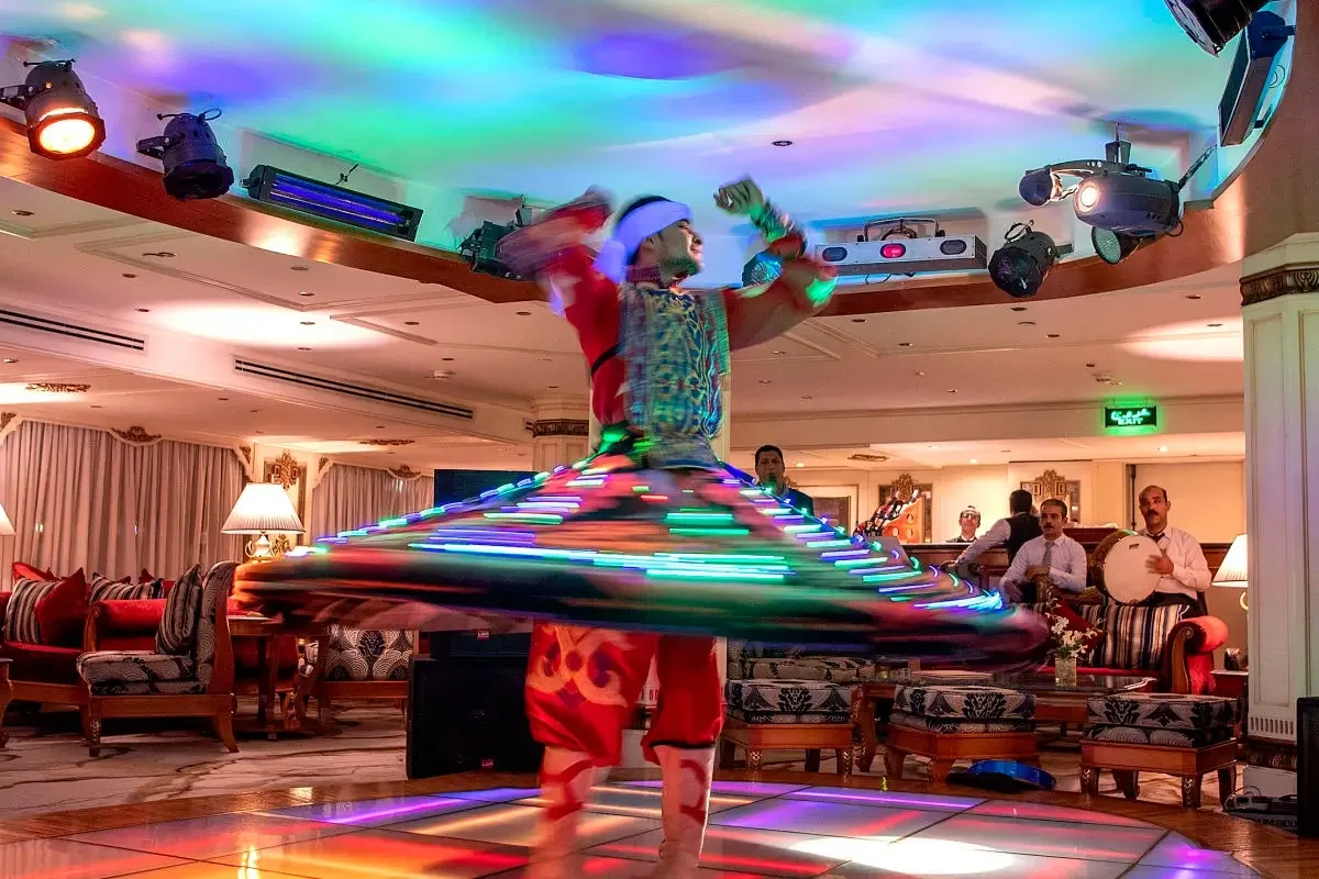 A tanoura dancer spinning in a lit skirt in the lounge of the Sonesta St. George I Nile cruise, guests watching from their seats