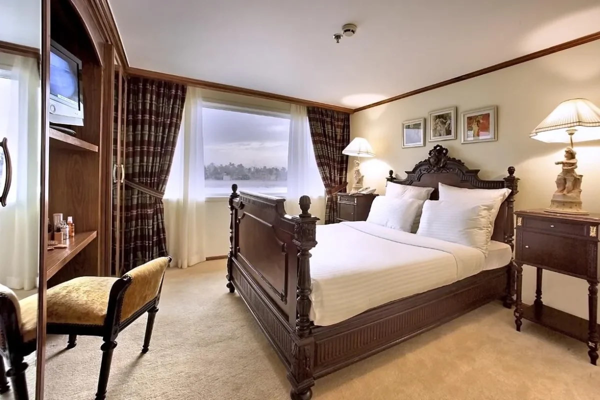 A double cabin on the Sonesta Star Goddess Nile cruise with a carved four-poster bed and framed prints on the wall