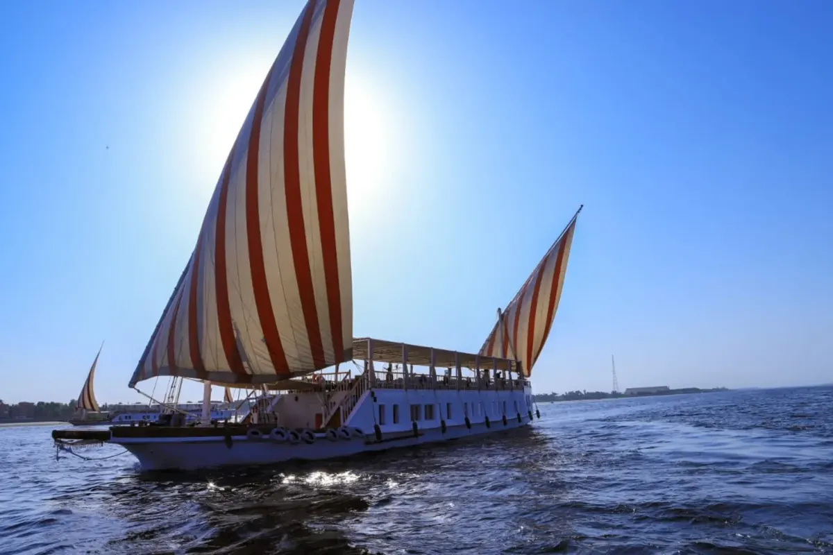 La dahabieh Three Pyramids sous des voiles rayées rouge et blanc sur le Nil