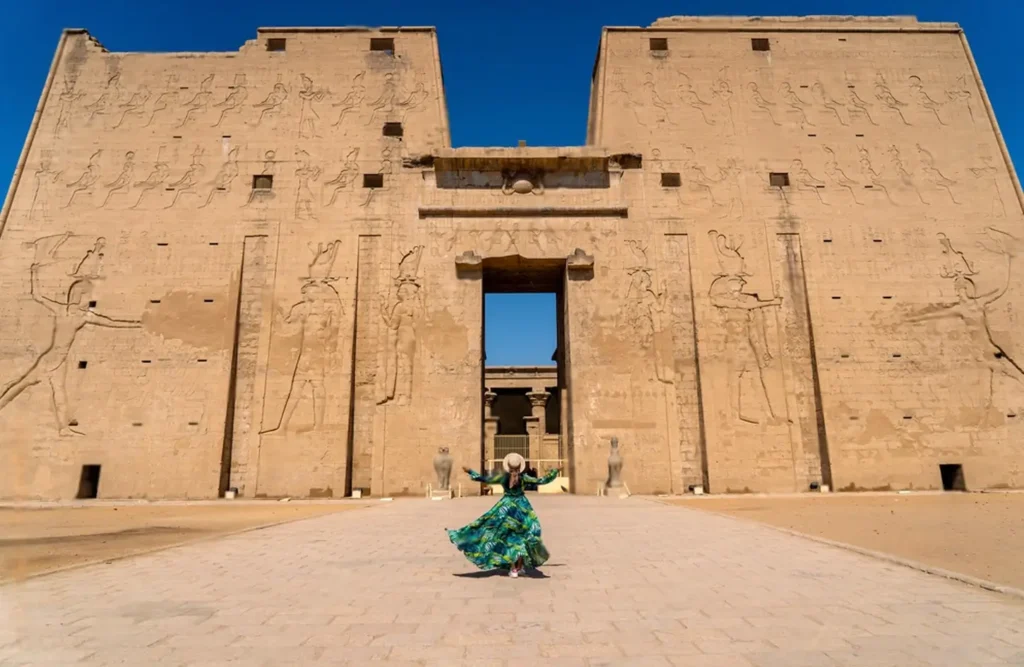 The towering pylon of the Temple of Horus at Edfu seen straight on from the forecourt, a visitor small at its centre
