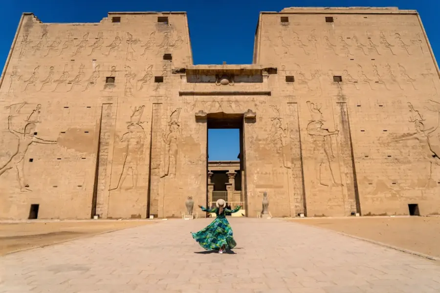 El imponente pilono del templo de Horus en Edfú visto de frente desde el patio, con un visitante diminuto en el centro