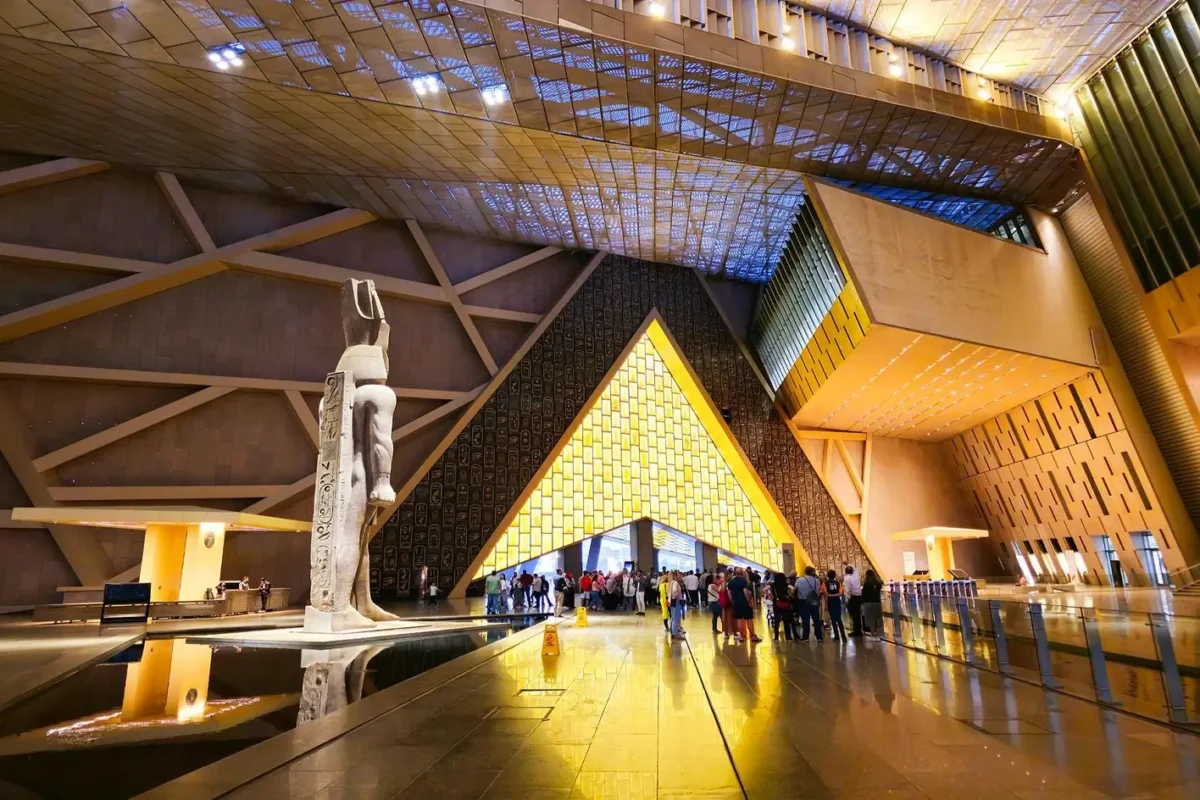 The colossal statue of Ramses II in the grand hall of the Grand Egyptian Museum, visitors queuing beneath the glazed roof
