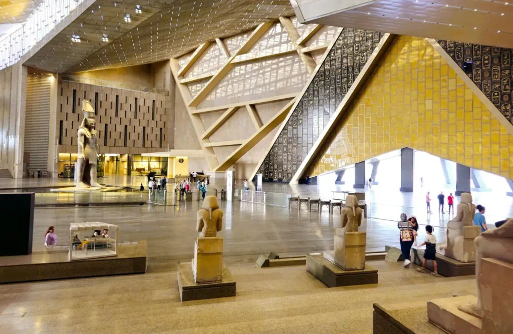 Estátuas ao longo da grande escadaria do Grande Museu Egípcio, com a luz do dia entrando pelas aberturas triangulares