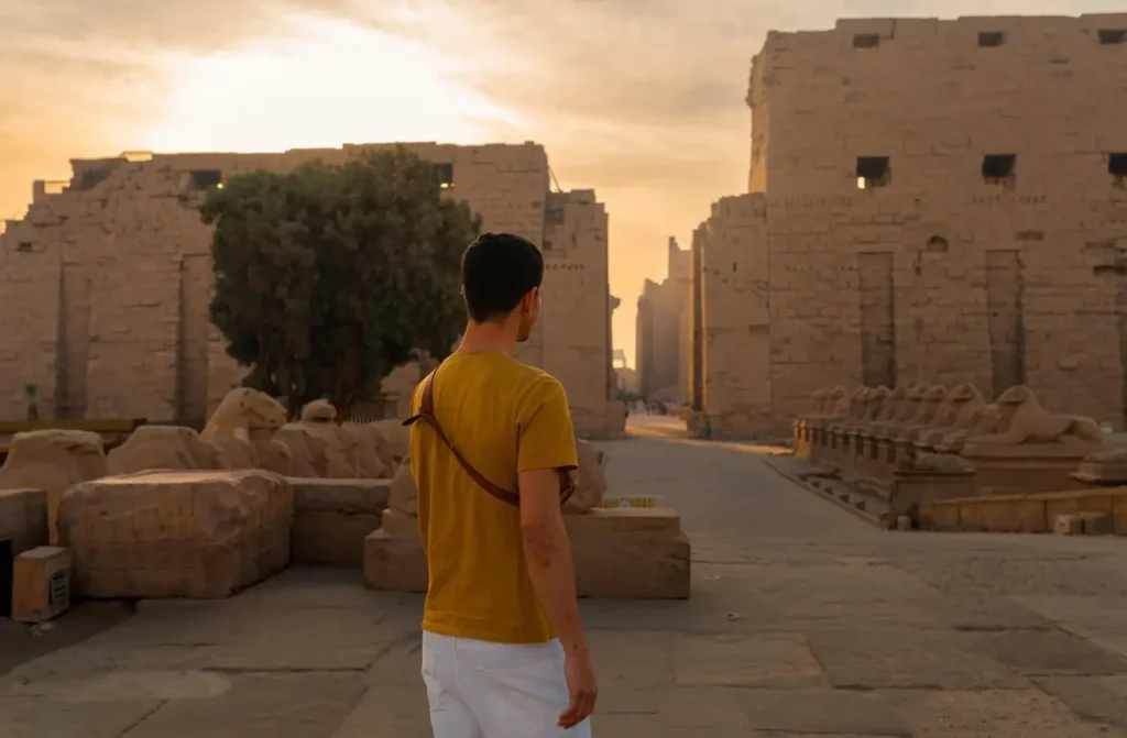 A visitor walking the ram-headed sphinx avenue at Karnak Temple in the low light of sunrise