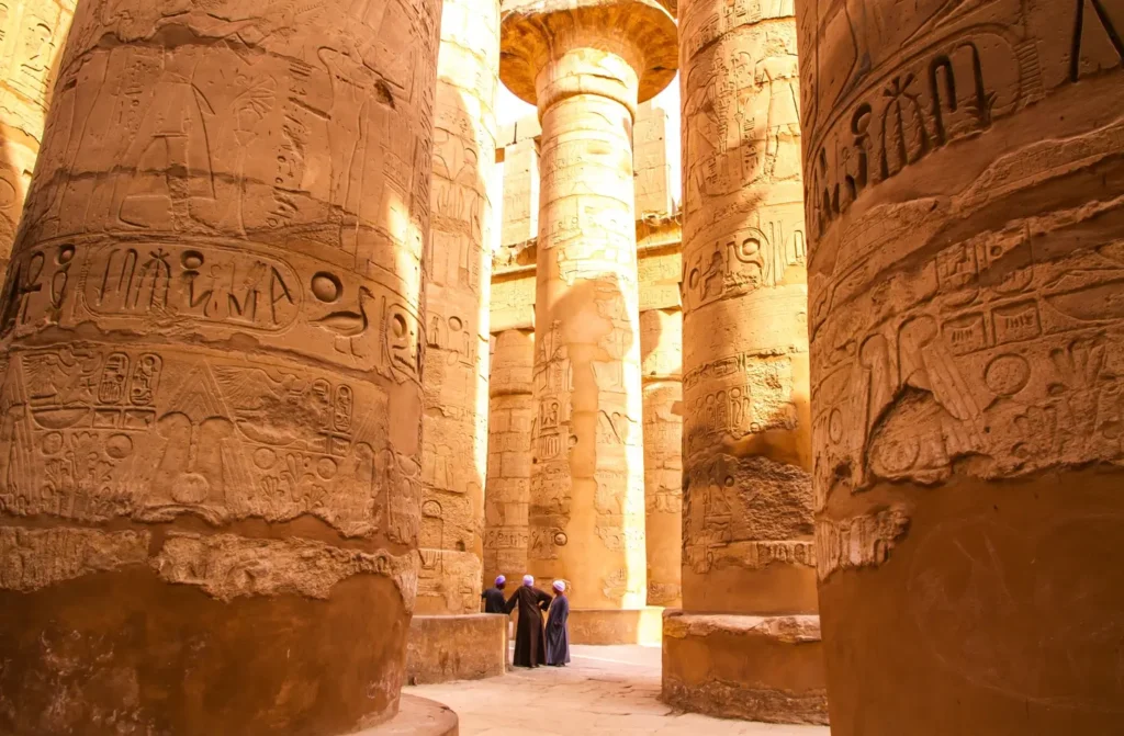 The carved sandstone columns of the great hypostyle hall at Karnak Temple, two visitors small between them