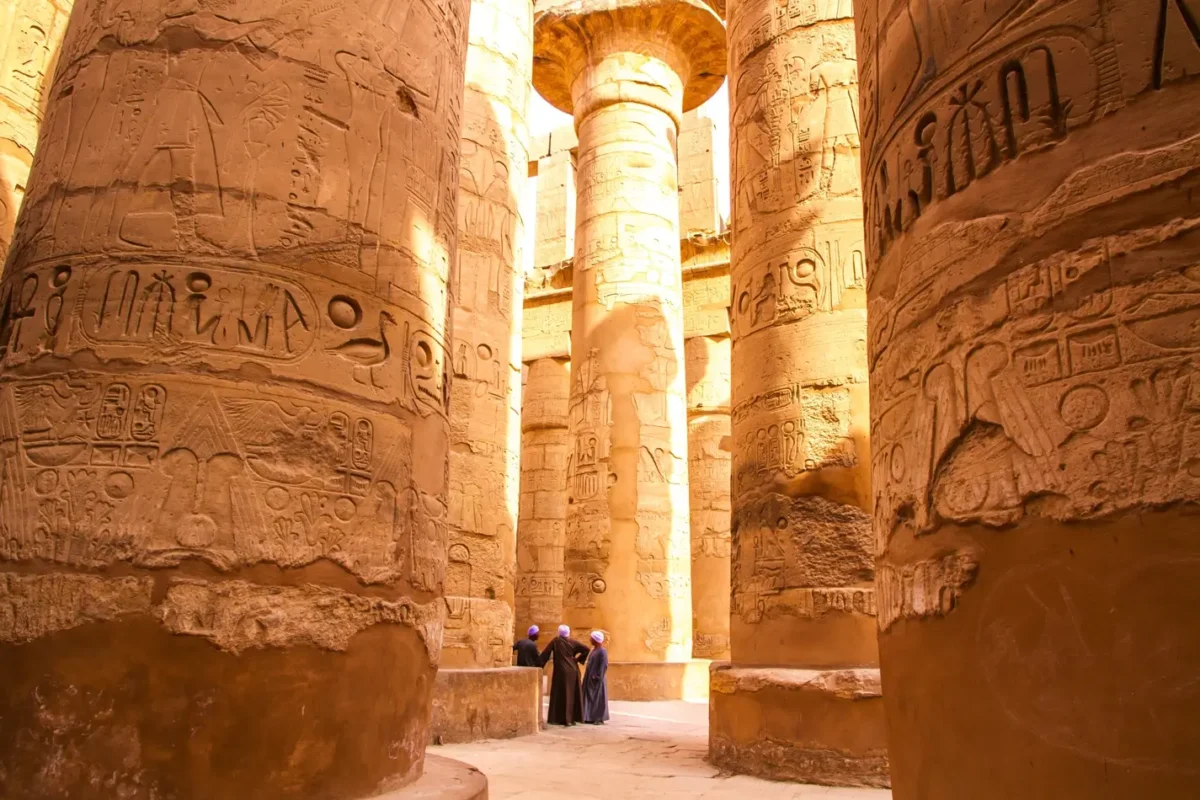 The carved sandstone columns of the great hypostyle hall at Karnak Temple, two visitors small between them