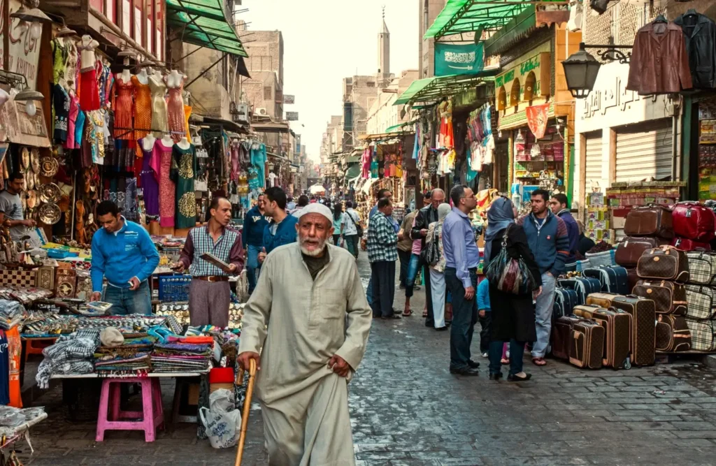 Shoppers and traders along a narrow market street in Khan el-Khalili, an elderly man in a galabeya walking towards the camera