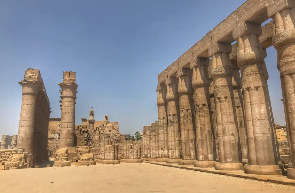The tall papyrus columns of the colonnade at Luxor Temple, the mosque of Abu Haggag rising behind them