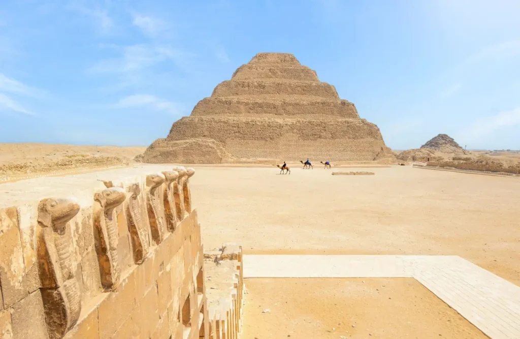 The Step Pyramid of Djoser seen across the great courtyard at Saqqara, riders on camels crossing the sand