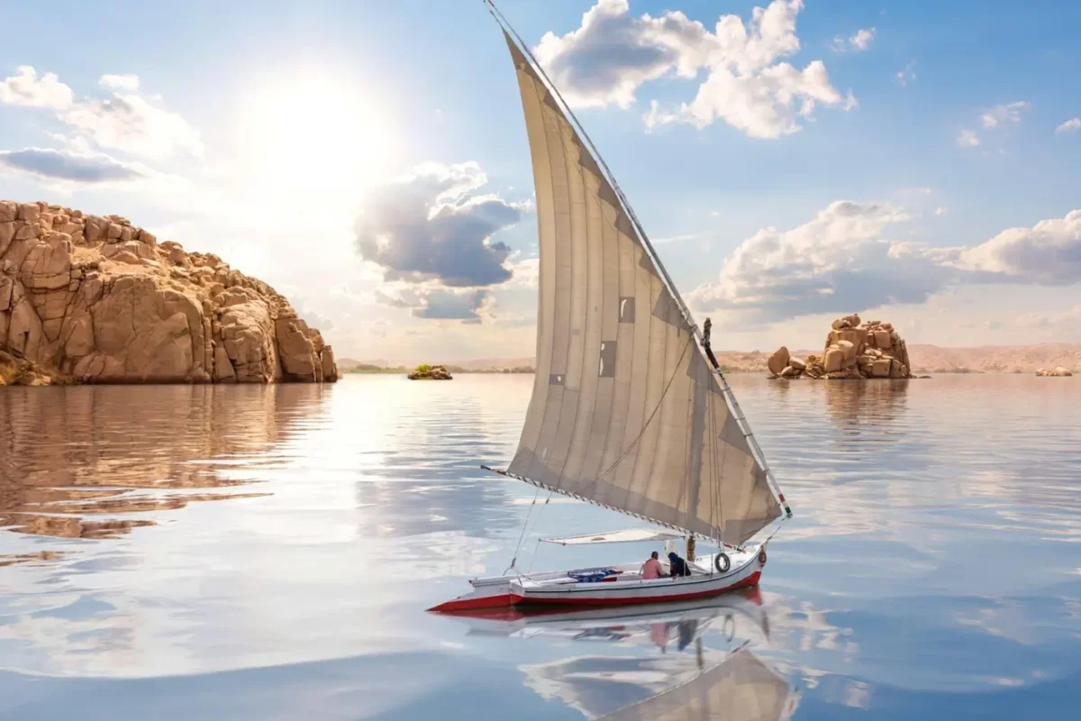 A felucca under full sail on still water at Aswan, granite outcrops rising from the river around it