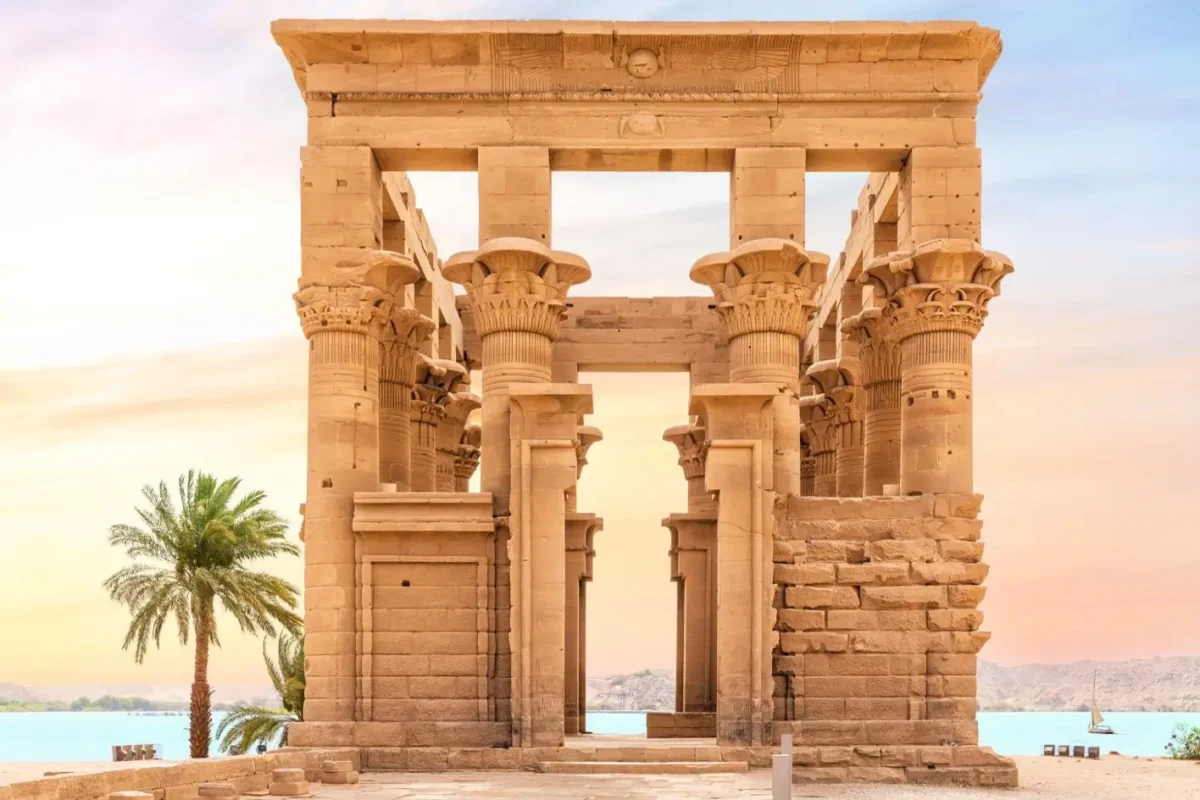The Kiosk of Trajan at Philae standing at the water's edge, a palm beside it in the evening light