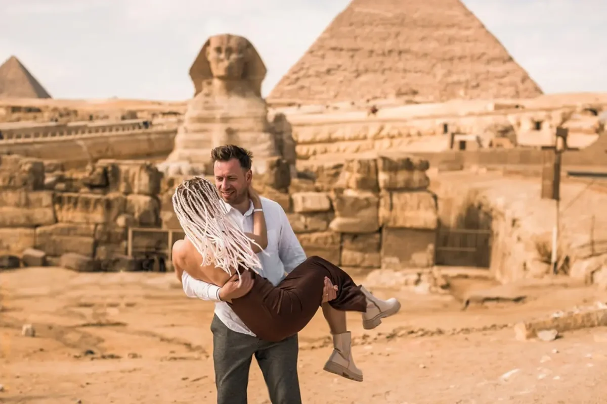 A man lifting a woman in front of the Great Sphinx and the pyramid of Khafre at Giza