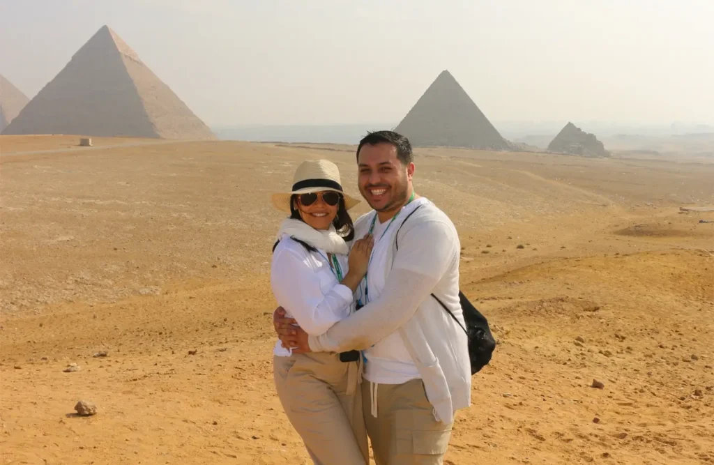 A couple embracing on the sand of the Giza plateau with the pyramids in the haze behind them