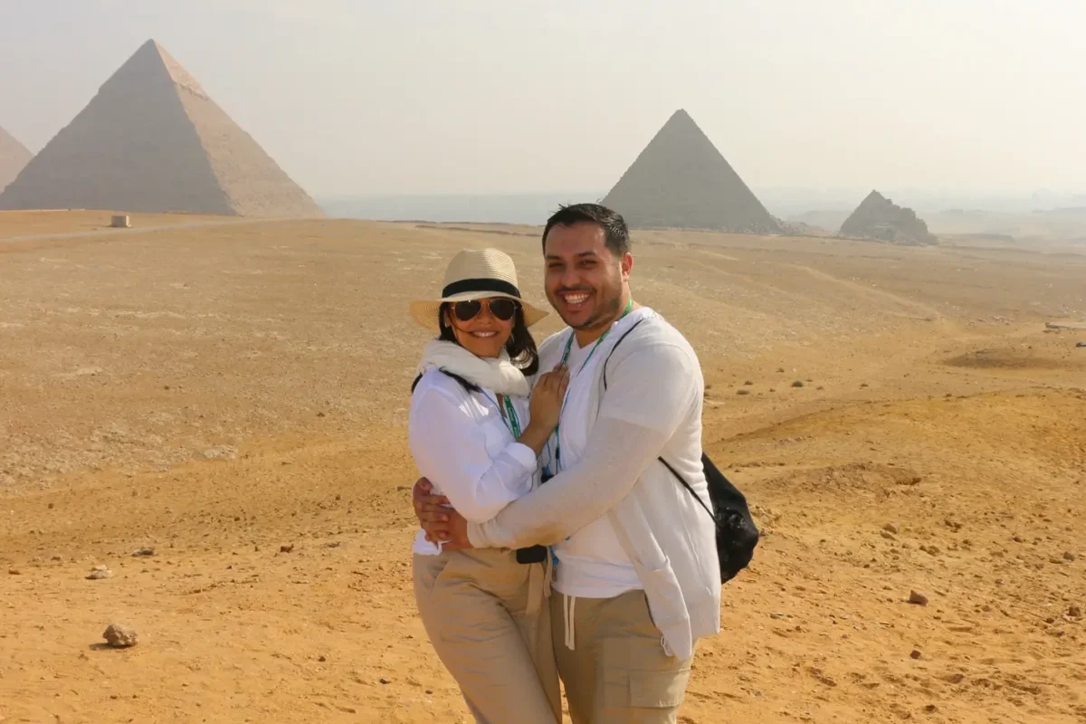 A couple embracing on the sand of the Giza plateau with the pyramids in the haze behind them