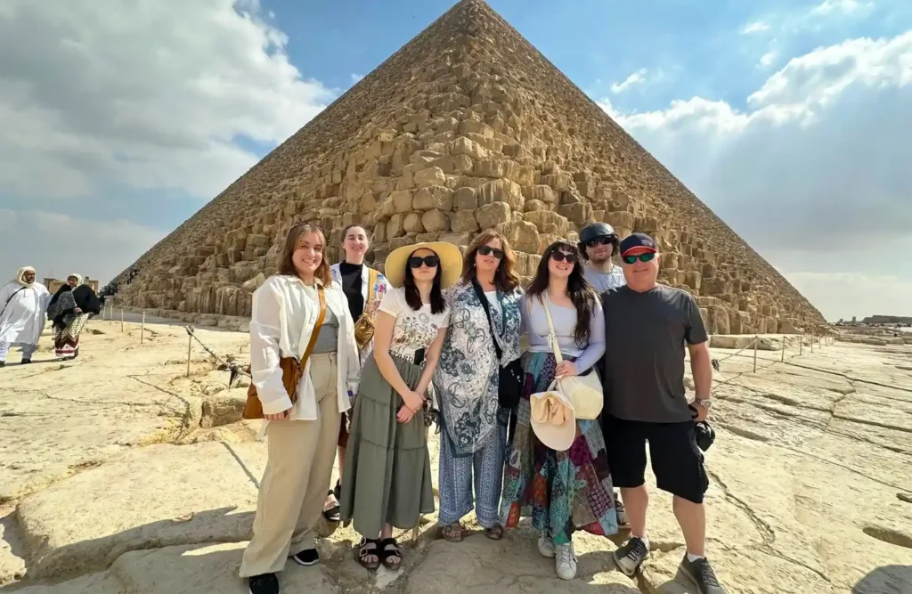 A group of visitors posing on the rock at the foot of the Great Pyramid of Khufu at Giza