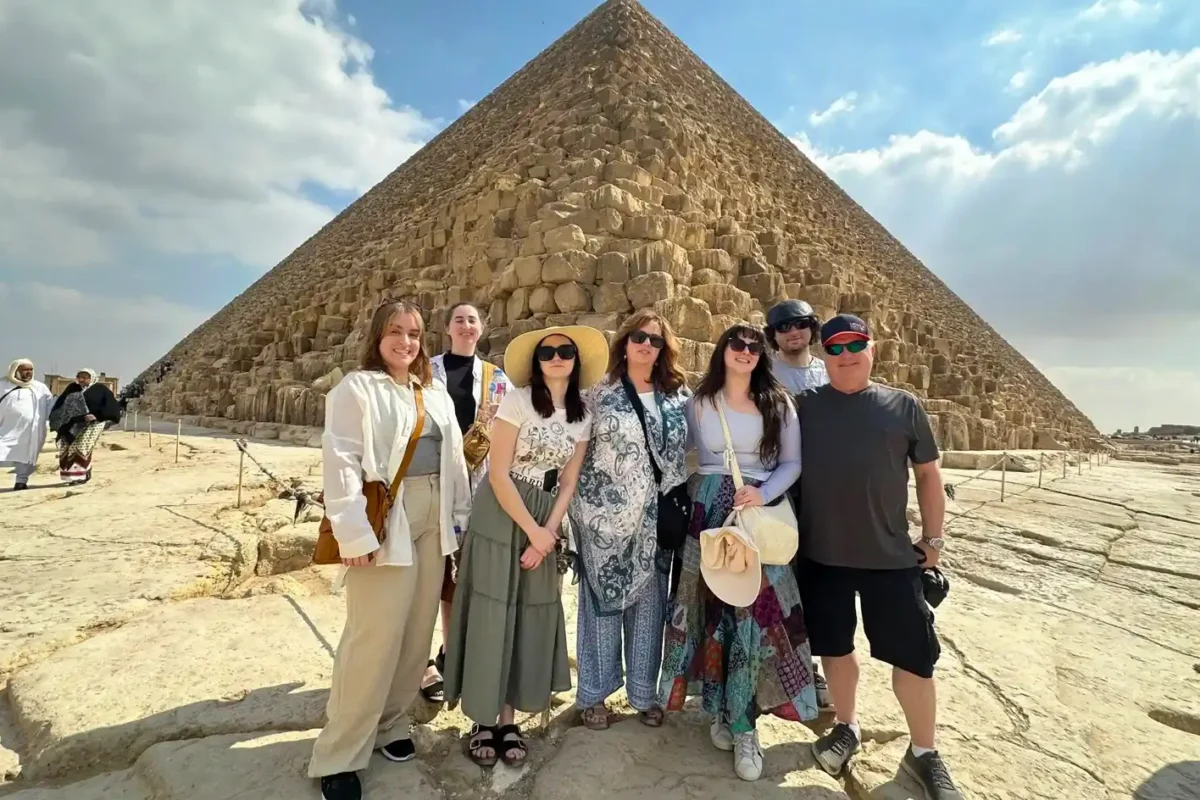 A group of visitors posing on the rock at the foot of the Great Pyramid of Khufu at Giza